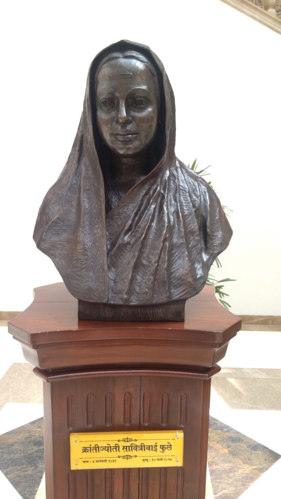 A bronze bust of Savitribai Phule with her sari drawn over her head, on a pedestal