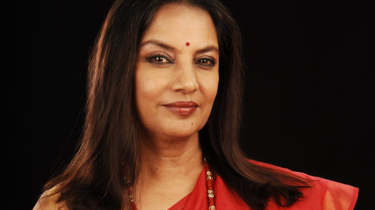 Portrait of Shabana Azmi in a red sari against a black background