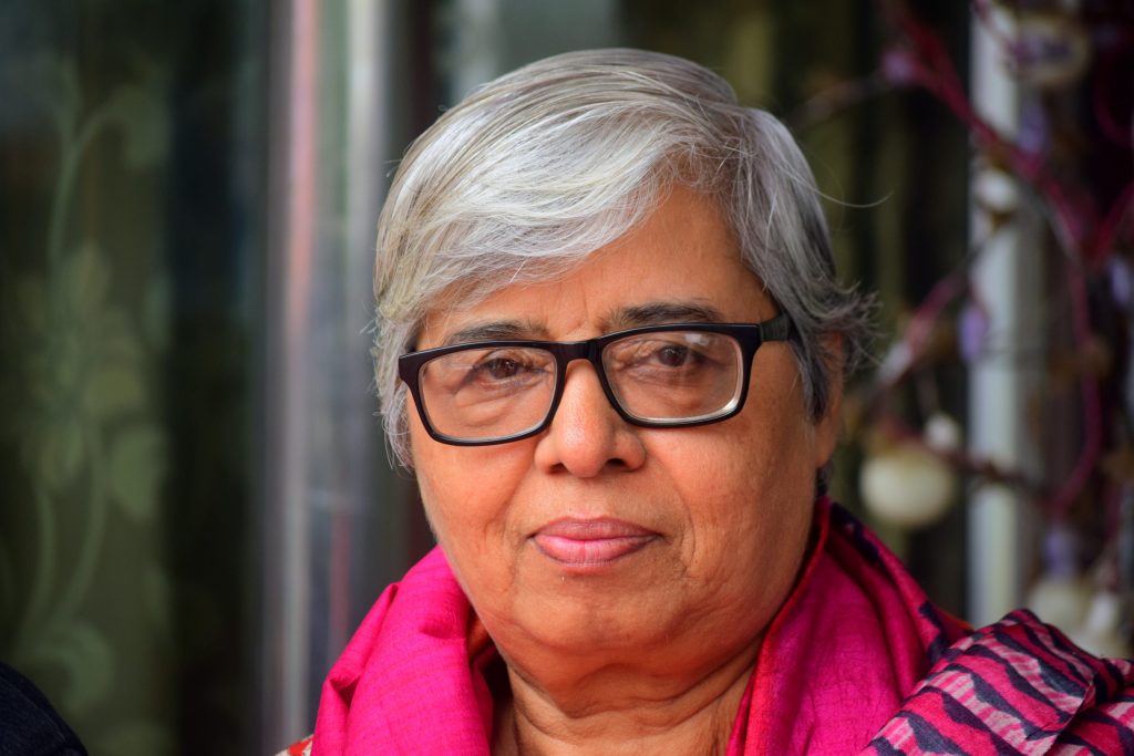 Close-up of Shabnam Hashmi with short grey hair, black-framed glasses and a pink scarf