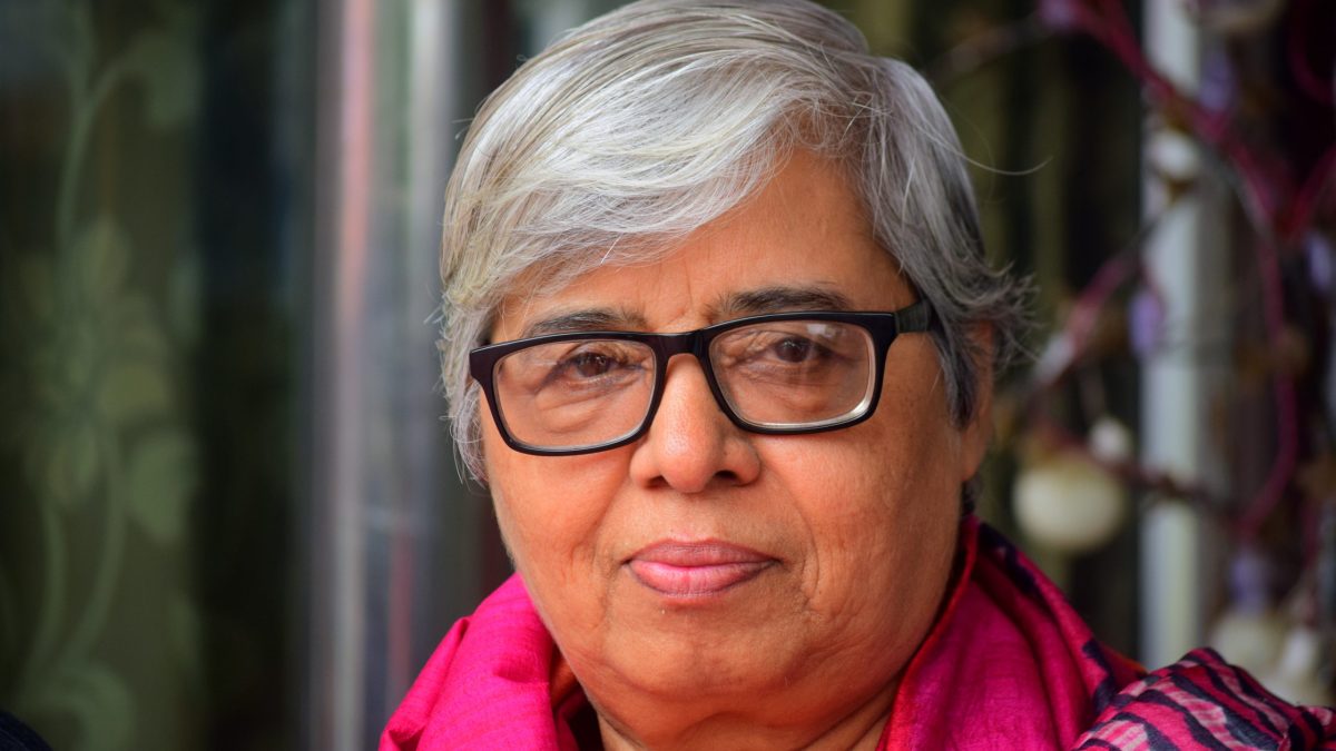 Close-up of Shabnam Hashmi with short grey hair, black-framed glasses and a pink scarf