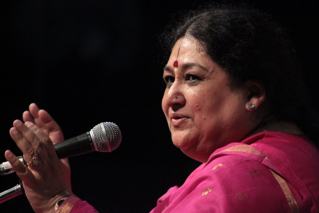 Shubha Mudgal in a pink sari singing into a microphone with one hand raised