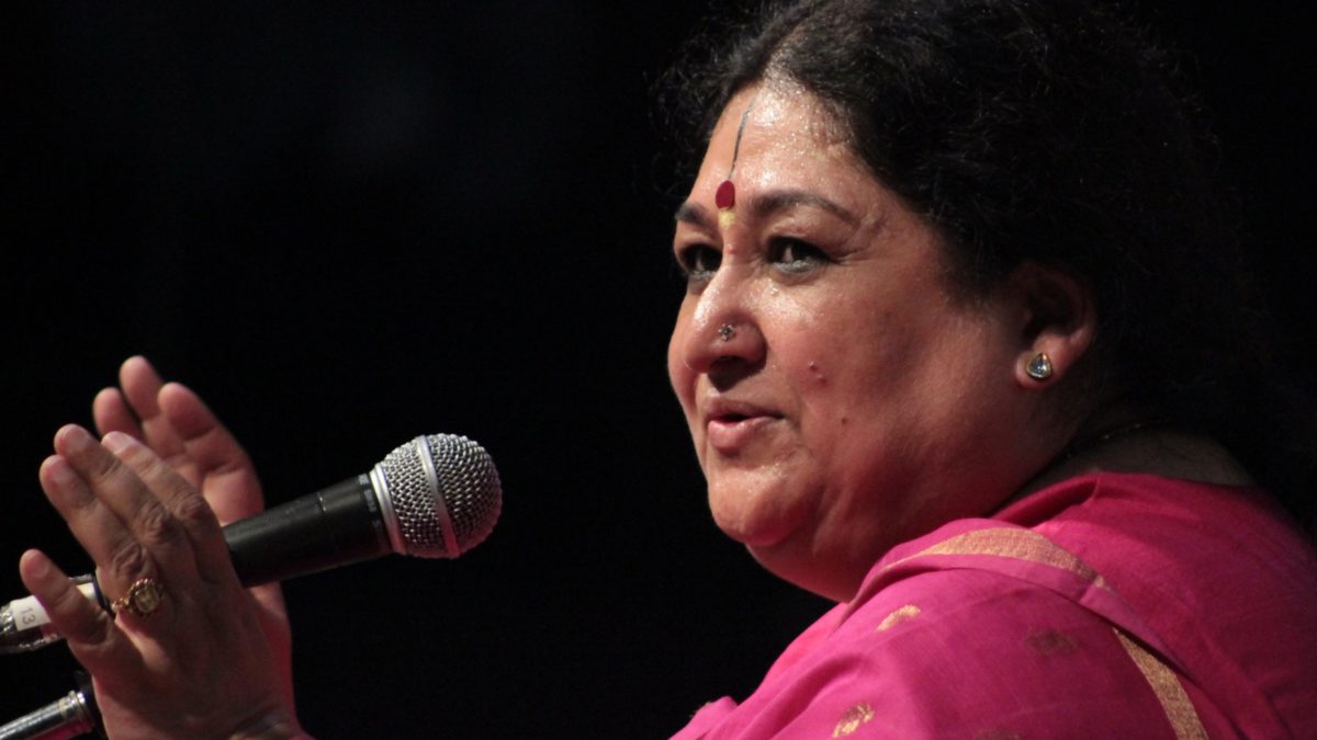 Shubha Mudgal in a pink sari singing into a microphone with one hand raised