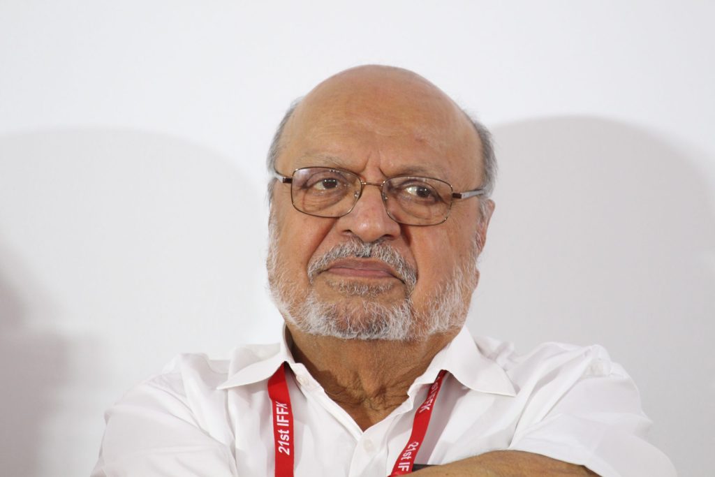 Close-up of Shyam Benegal with a white beard and glasses, wearing a festival lanyard