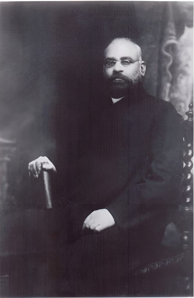 Shyamji Krishna Varma seated in a dark suit, with a beard and glasses