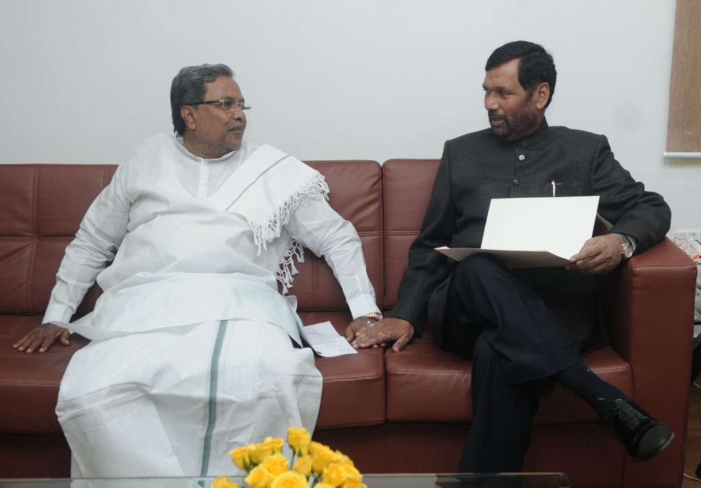 Siddaramaiah in a white shirt and dhoti seated in conversation with Ram Vilas Paswan