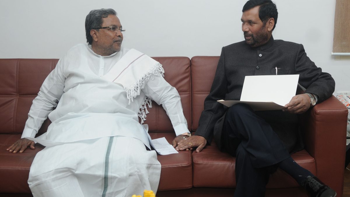 Siddaramaiah in a white shirt and dhoti seated in conversation with Ram Vilas Paswan