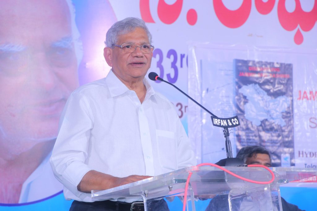 Sitaram Yechury with grey hair in a white kurta speaking at a lectern