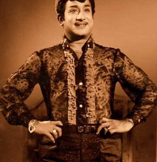 Sivaji Ganesan standing with his hands on his hips, in a patterned shirt
