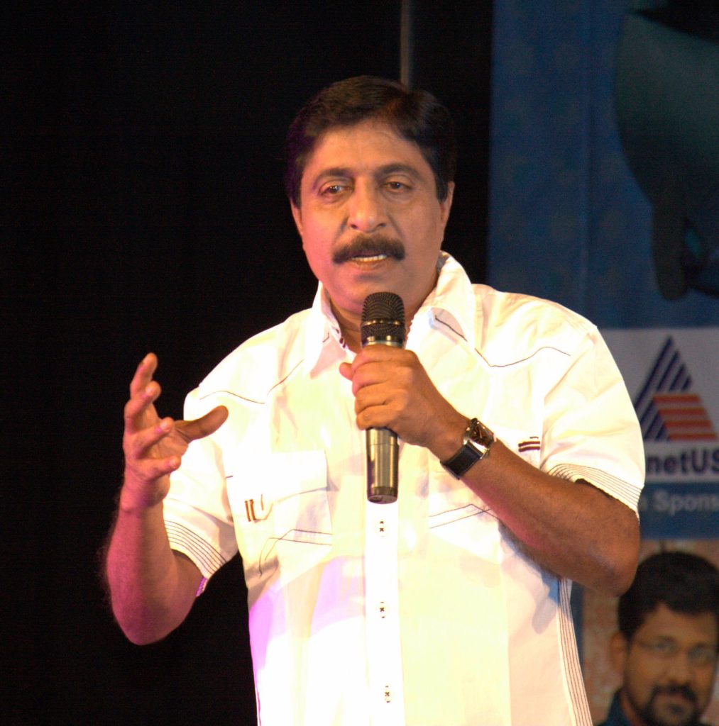 Sreenivasan in a yellow printed shirt speaking into a microphone on stage