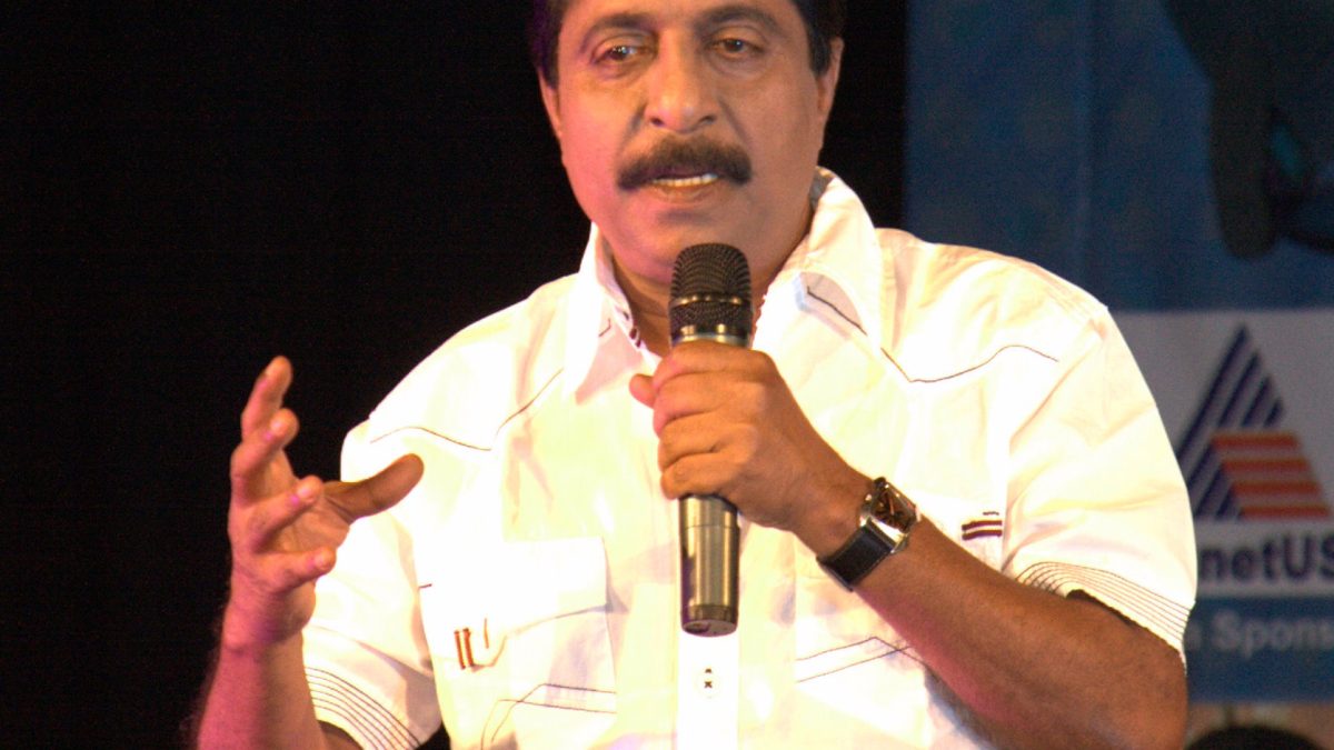 Sreenivasan in a yellow printed shirt speaking into a microphone on stage