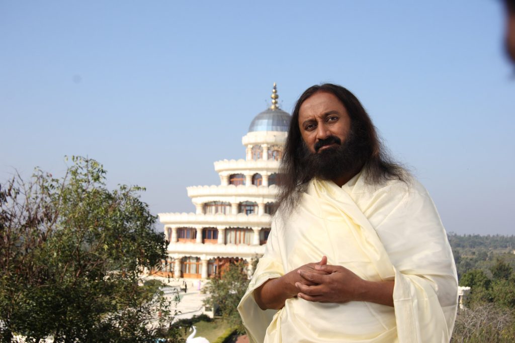 Sri Sri Ravi Shankar with long hair and beard, in white robes, standing outdoors