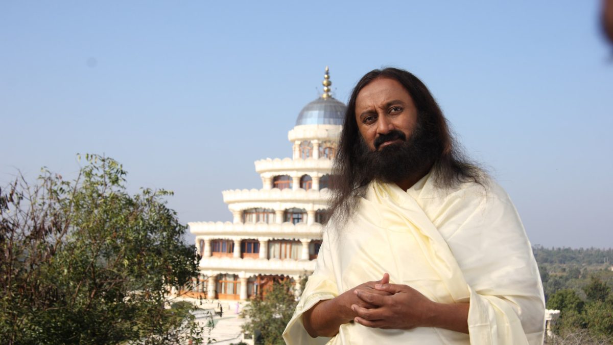 Sri Sri Ravi Shankar with long hair and beard, in white robes, standing outdoors