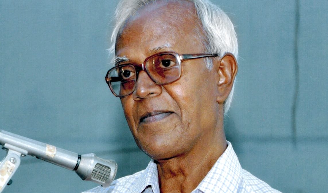 Stan Swamy with white hair and glasses speaking into a microphone
