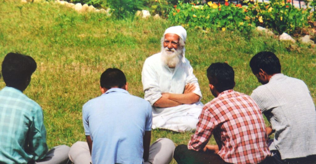 Sunderlal Bahuguna in white, seated on the grass talking with a group of people