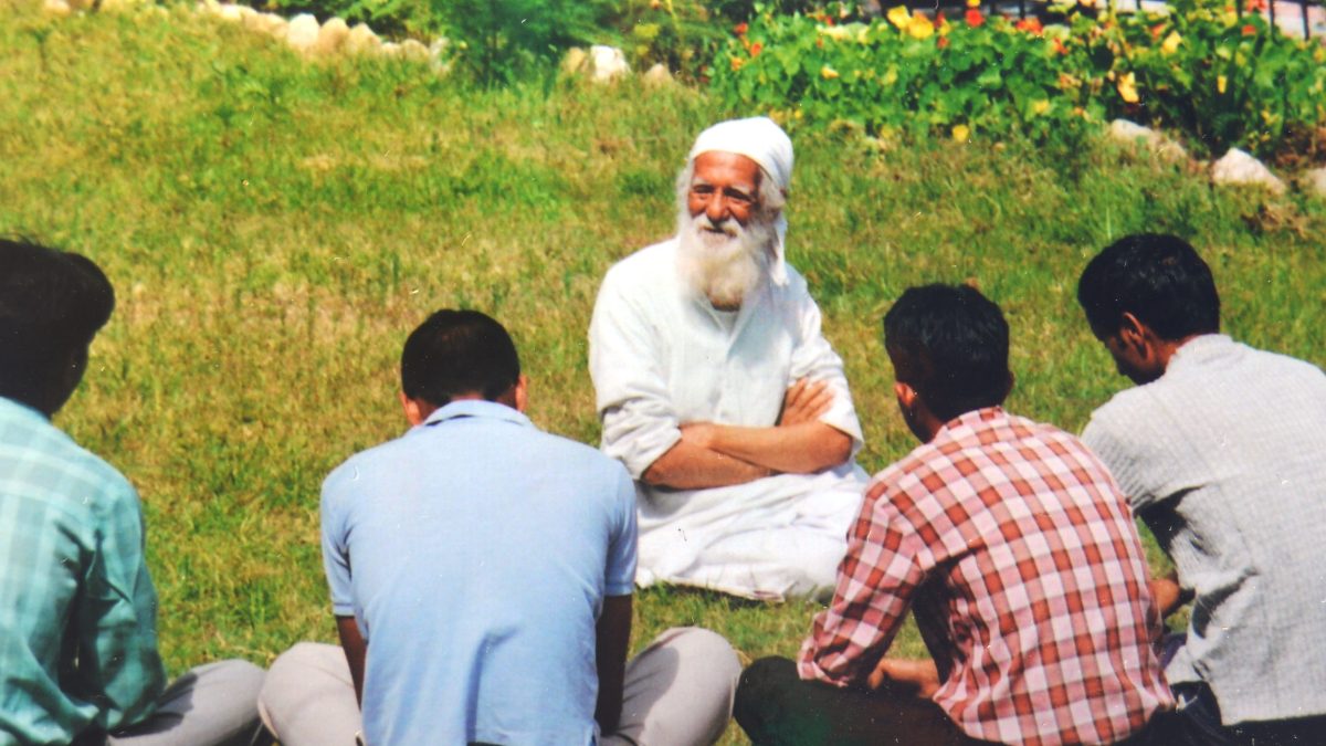 Sunderlal Bahuguna in white, seated on the grass talking with a group of people