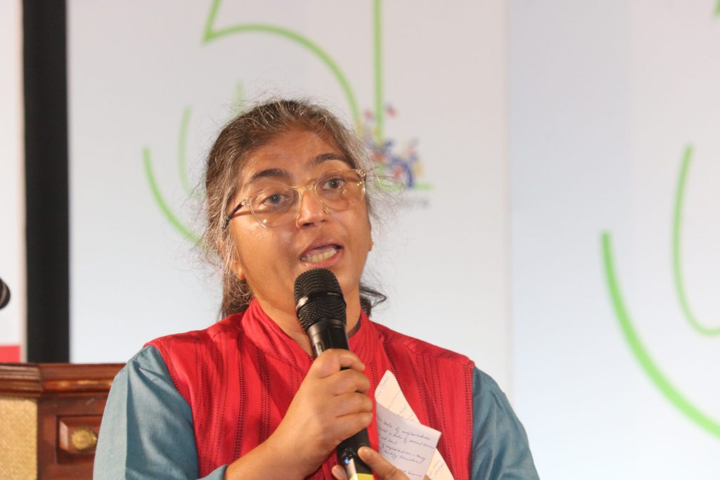 Sunitha Krishnan in glasses and a red jacket speaking into a microphone