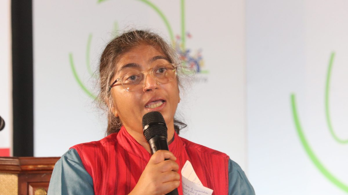 Sunitha Krishnan in glasses and a red jacket speaking into a microphone