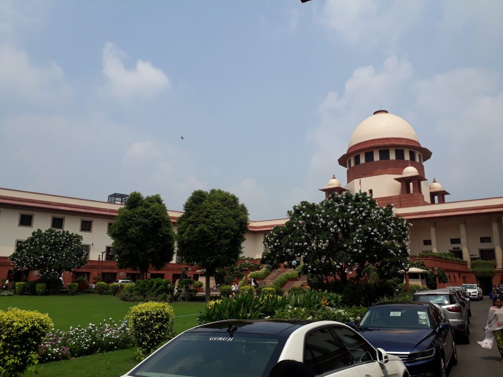 The Supreme Court of India building with its dome behind trees and parked cars