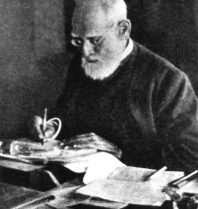 A black-and-white photograph of the elderly Surendranath Banerjee writing at a desk