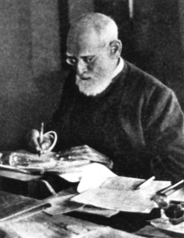 A black-and-white photograph of the elderly Surendranath Banerjee writing at a desk