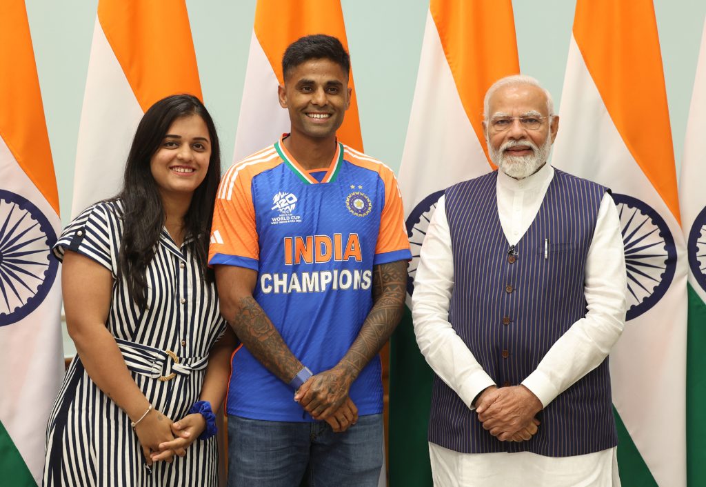 Suryakumar Yadav in India's champions jersey standing between his wife and Prime Minister Narendra Modi