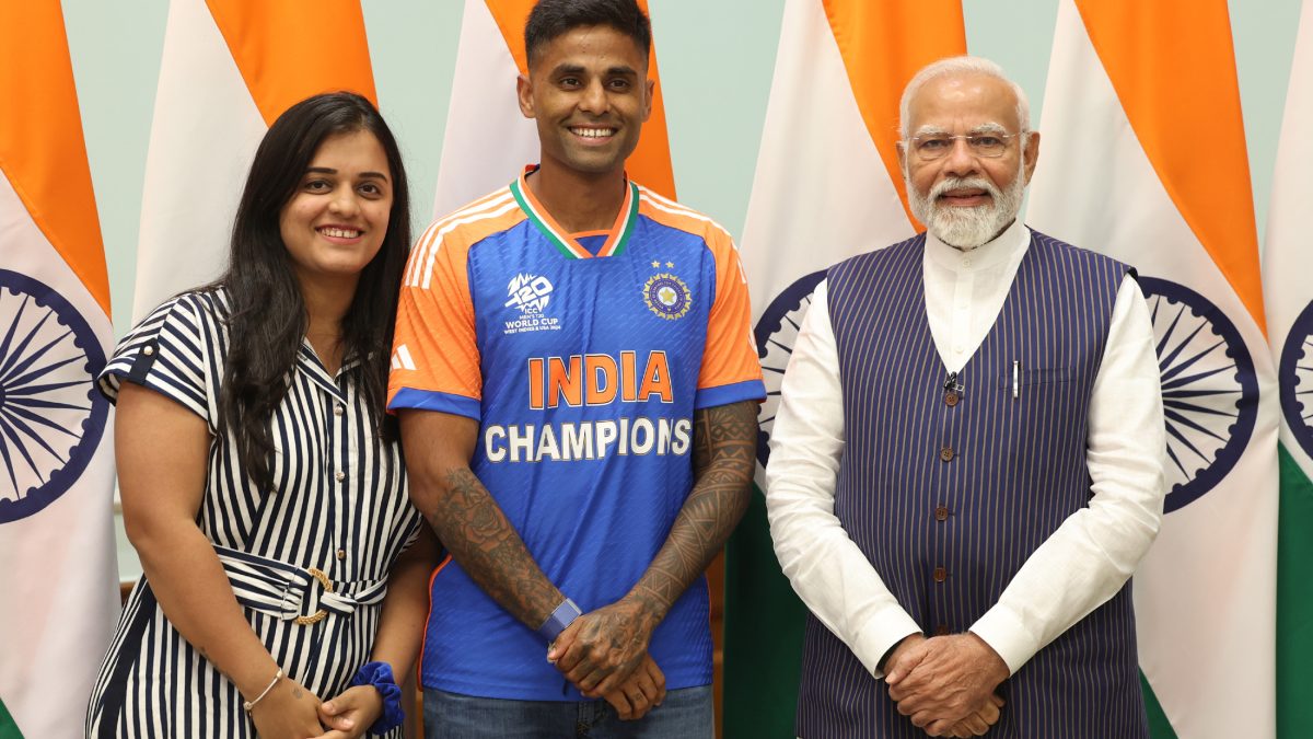 Suryakumar Yadav in India's champions jersey standing between his wife and Prime Minister Narendra Modi