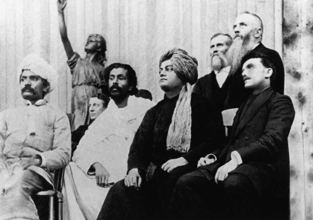 Swami Vivekananda in turban and robe seated on the platform at the Parliament of Religions in Chicago