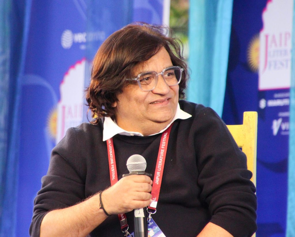 Swanand Kirkire in glasses and a dark jacket, smiling as he holds a microphone