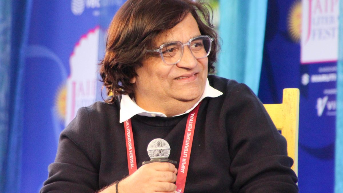 Swanand Kirkire in glasses and a dark jacket, smiling as he holds a microphone