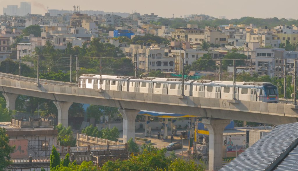 A Hyderabad Metro train on an elevated viaduct above a residential area