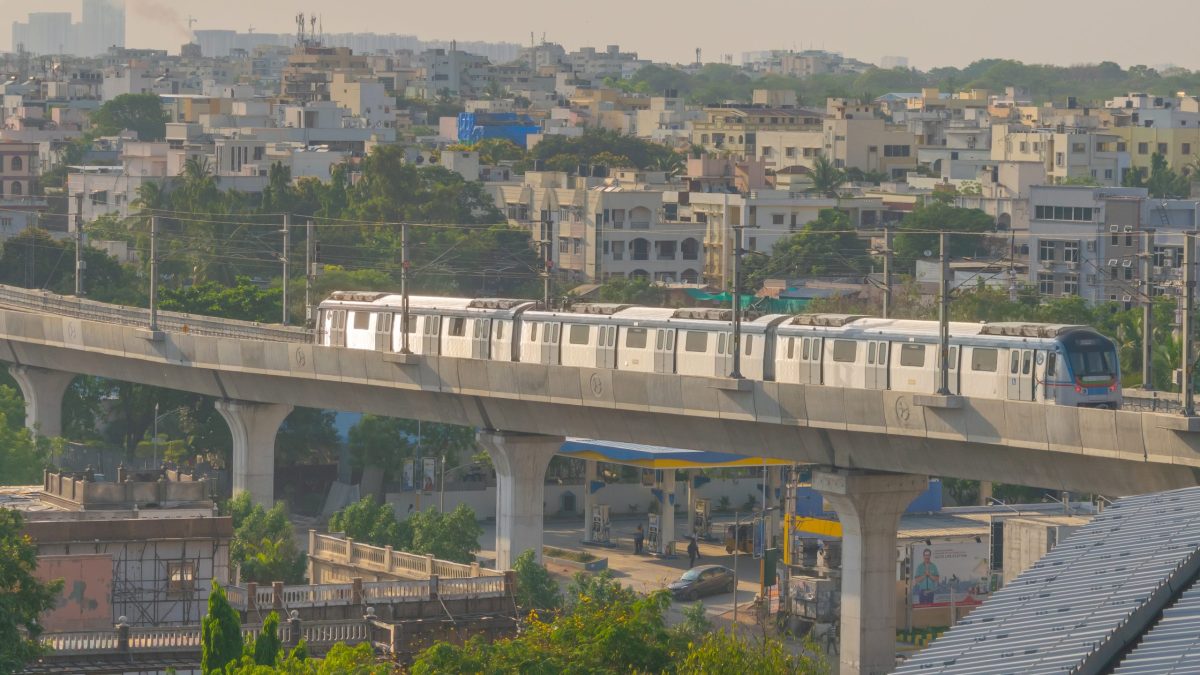 A Hyderabad Metro train on an elevated viaduct above a residential area