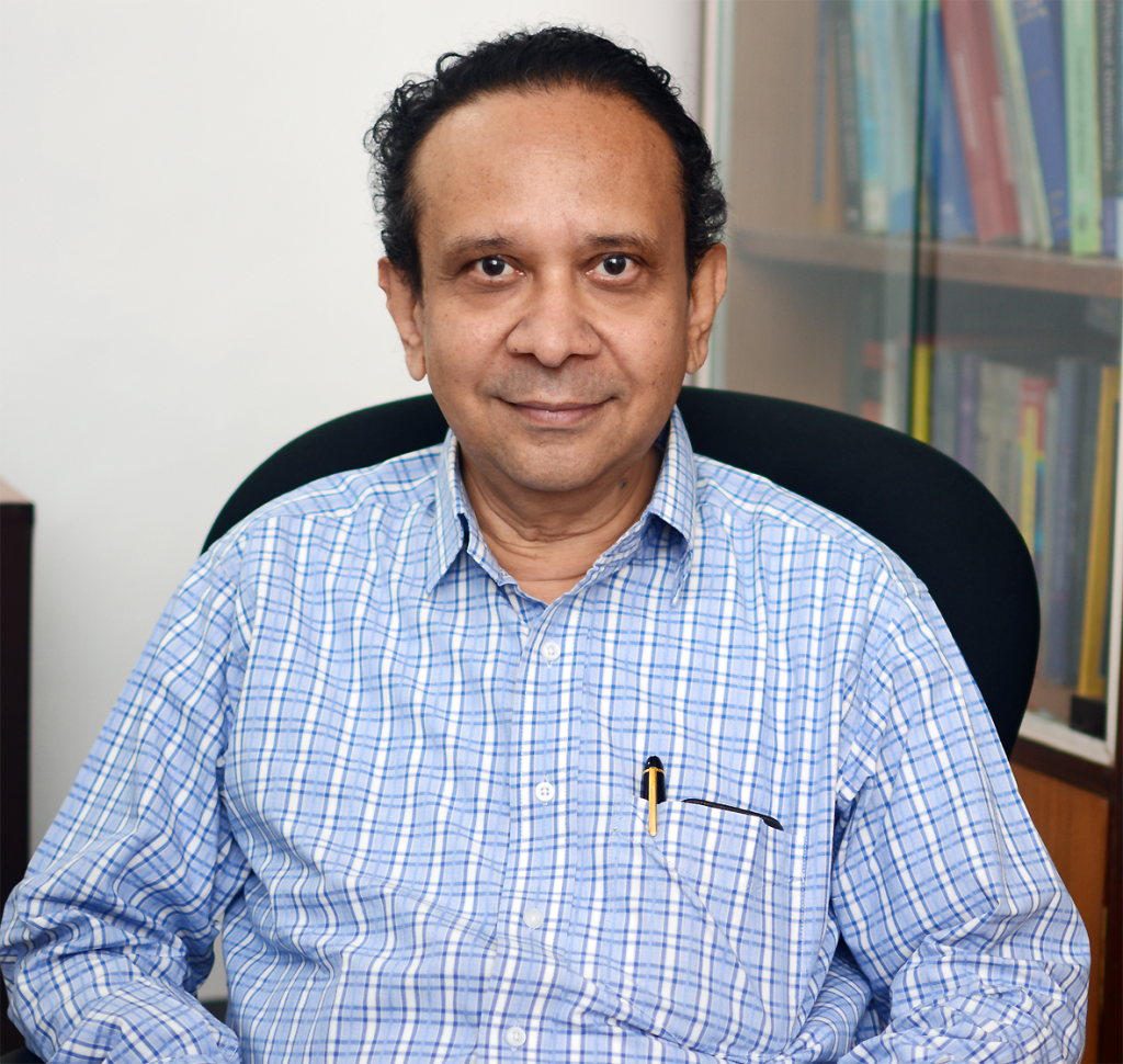 Thanu Padmanabhan in a blue checked shirt seated in his office, smiling