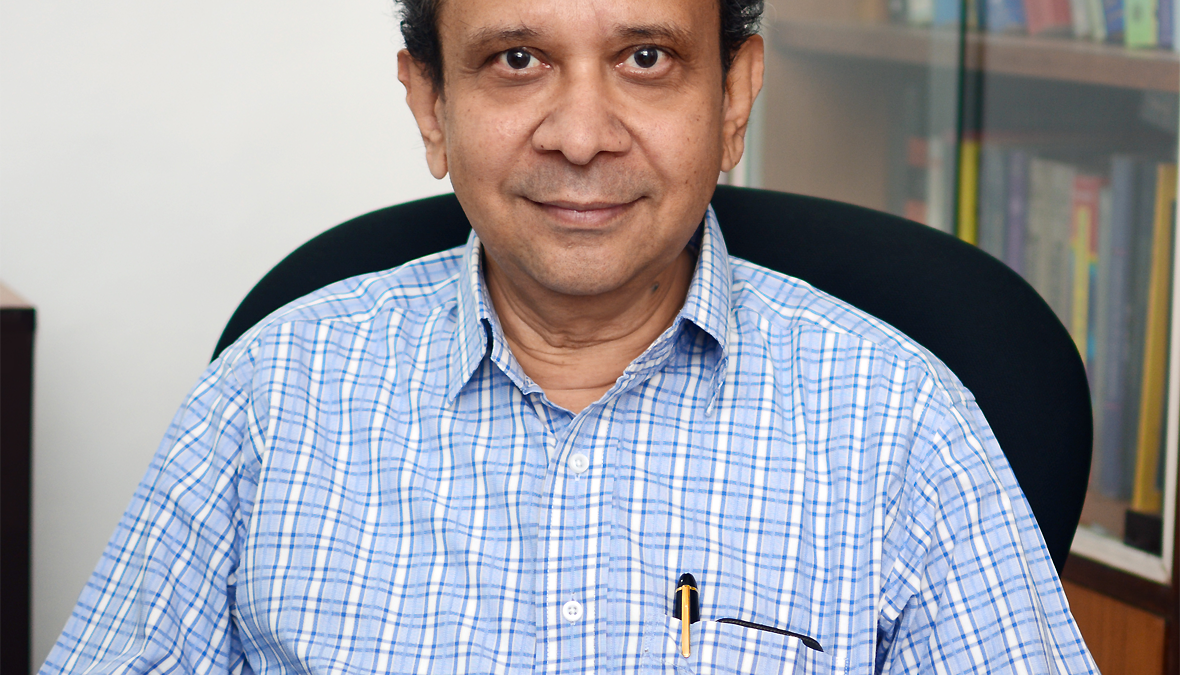Thanu Padmanabhan in a blue checked shirt seated in his office, smiling