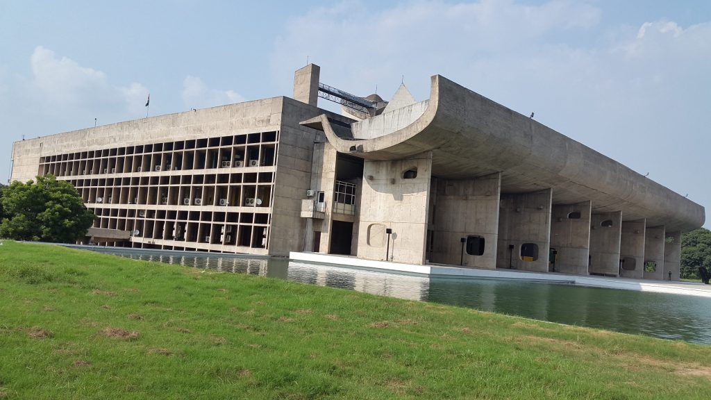 The long concrete buildings of the Capitol Complex in Chandigarh seen across a lawn