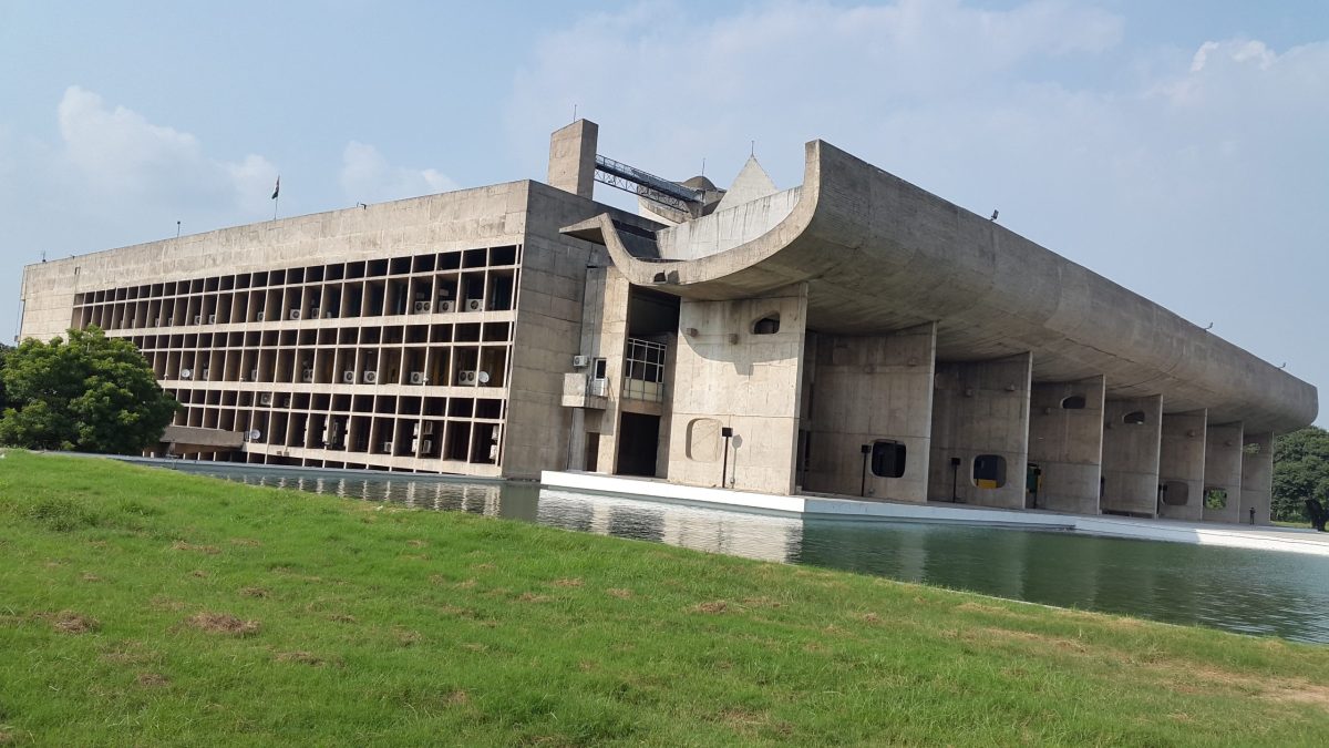 The long concrete buildings of the Capitol Complex in Chandigarh seen across a lawn