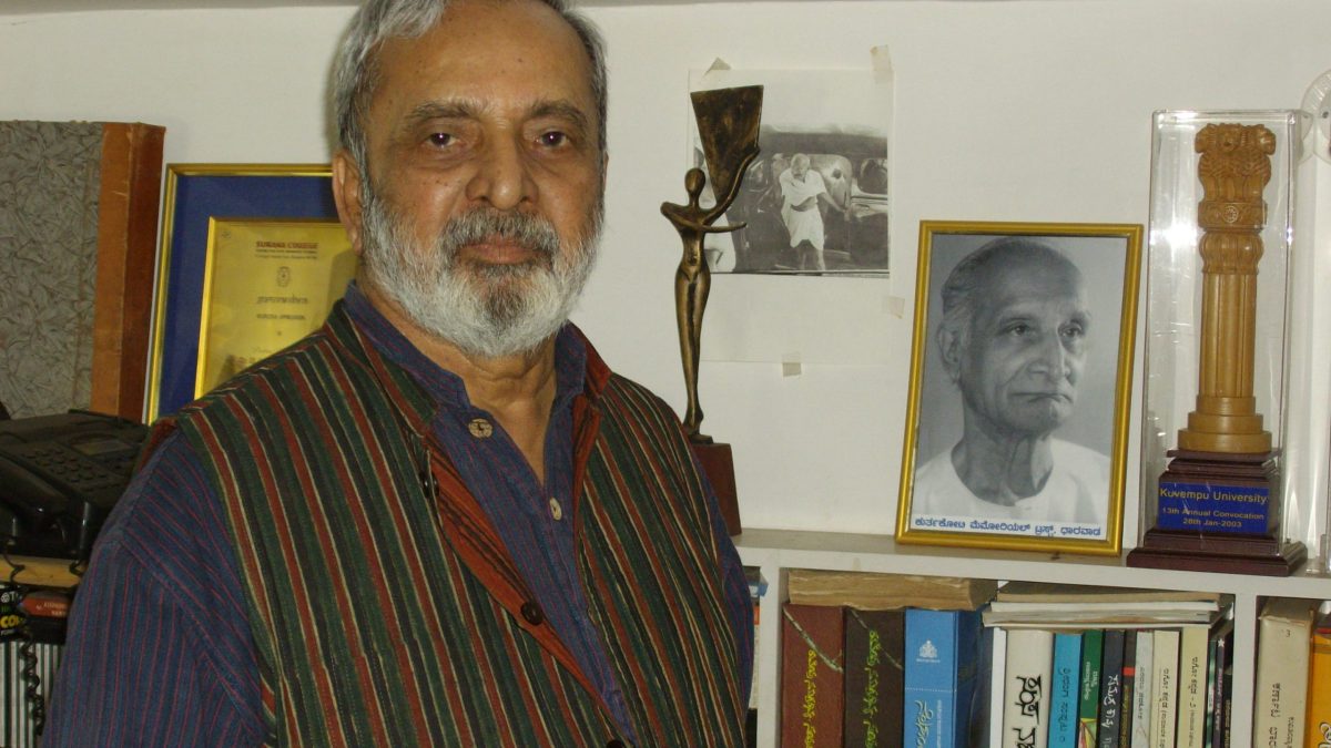 U. R. Ananthamurthy with a grey beard, in a striped waistcoat, standing before bookshelves