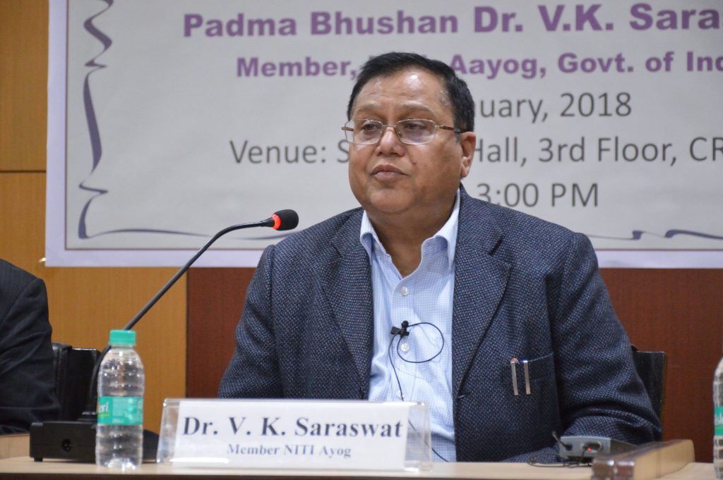 V. K. Saraswat in glasses and a dark suit seated at a table with a microphone