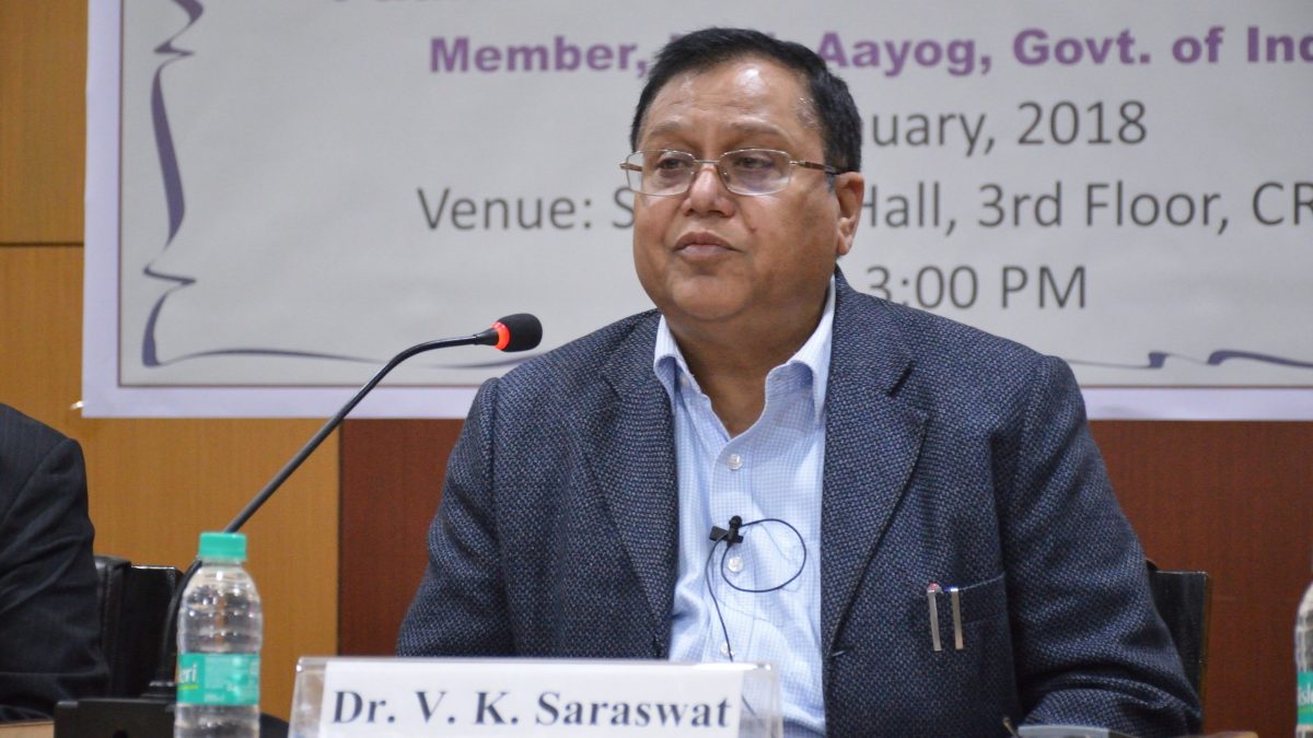 V. K. Saraswat in glasses and a dark suit seated at a table with a microphone
