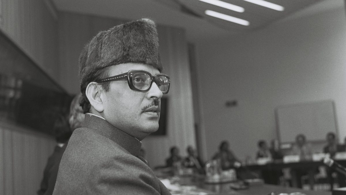 Black-and-white photograph of V. P. Singh in a fur cap and glasses seated at a conference table