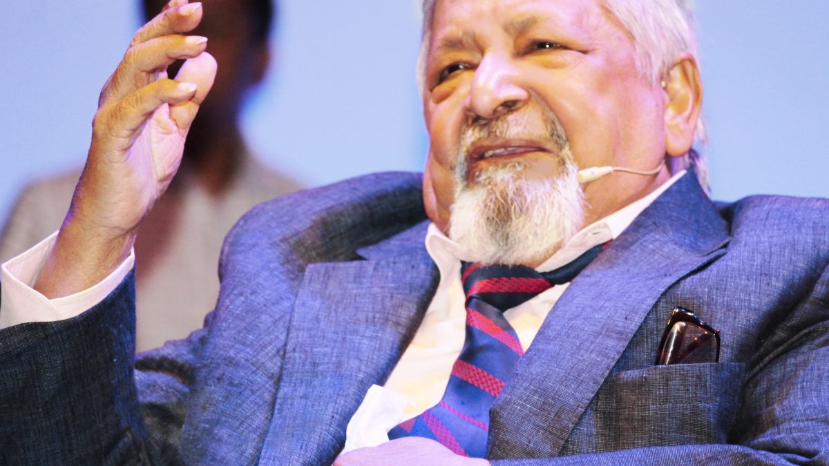 V. S. Naipaul seated, speaking into a microphone