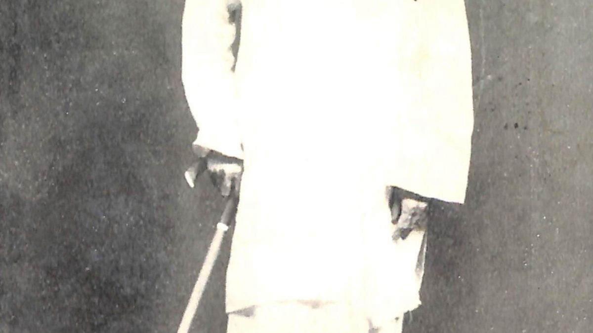 Full-length black-and-white photograph of Vallathol in a white shirt and mundu, holding a walking stick