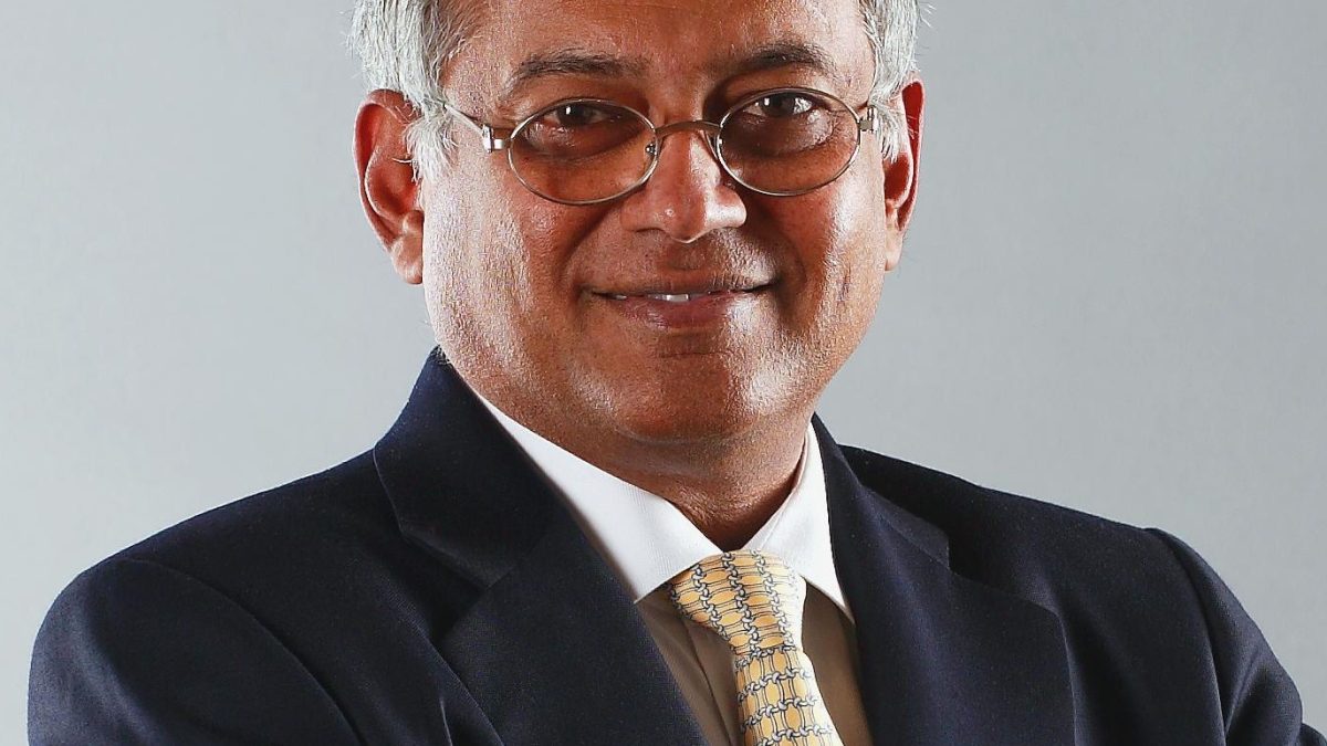 Venu Srinivasan in glasses, a dark suit and yellow tie