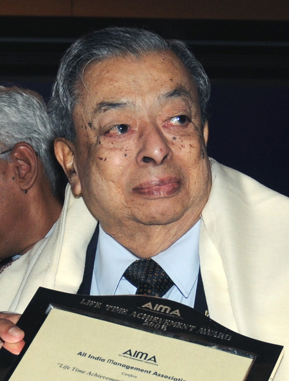 An elderly Verghese Kurien in a suit and shawl holding a citation