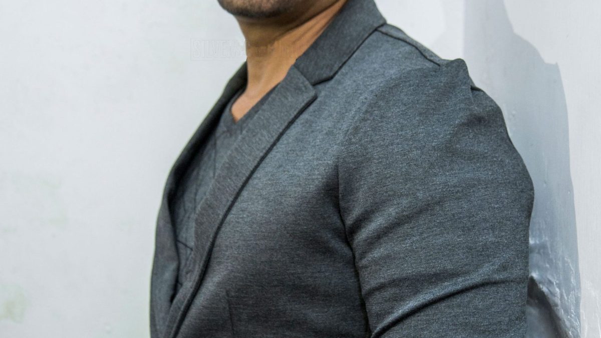 Vikram with a moustache, in a grey jacket, standing with his hands in his pockets