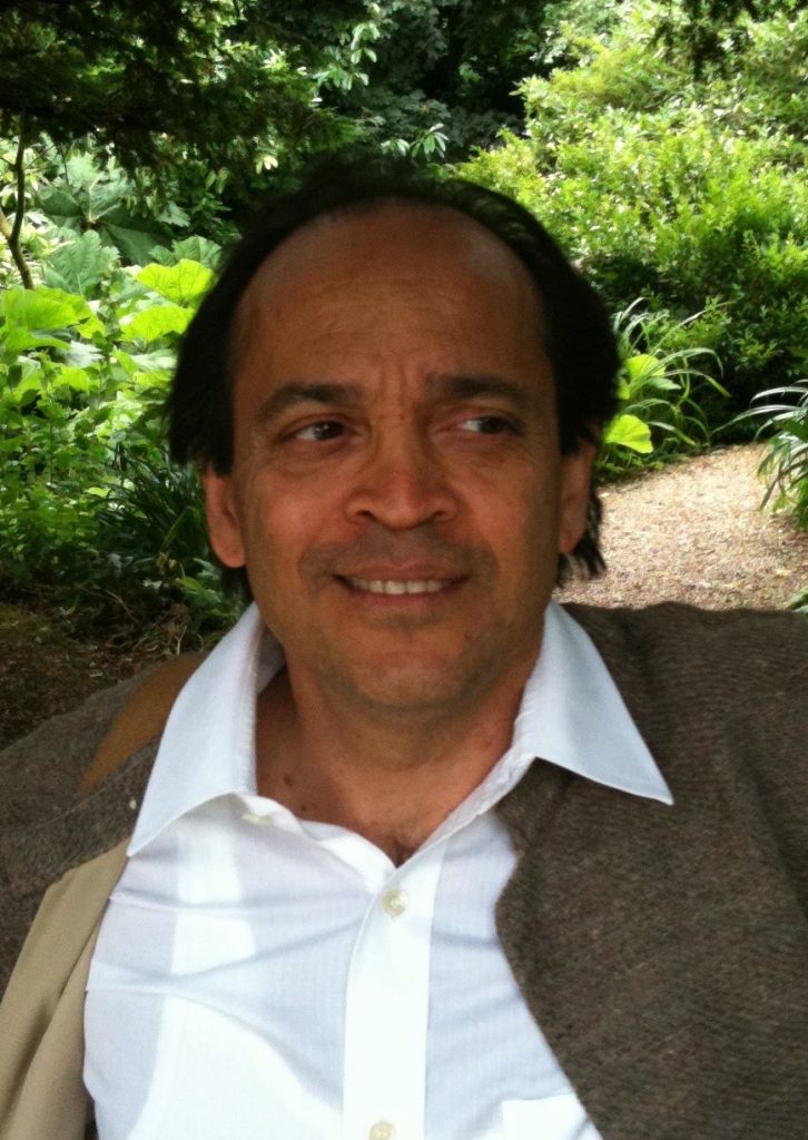 Vikram Seth smiling, in a jacket and open-necked shirt, in a garden