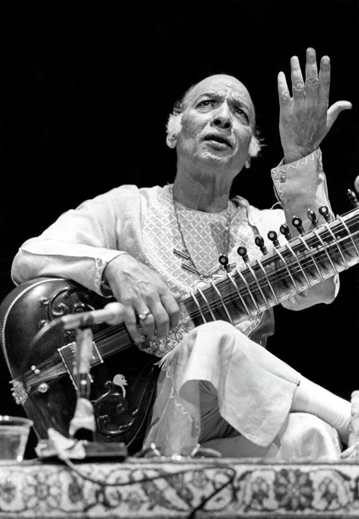 A black-and-white photograph of Vilayat Khan playing the sitar, one hand raised