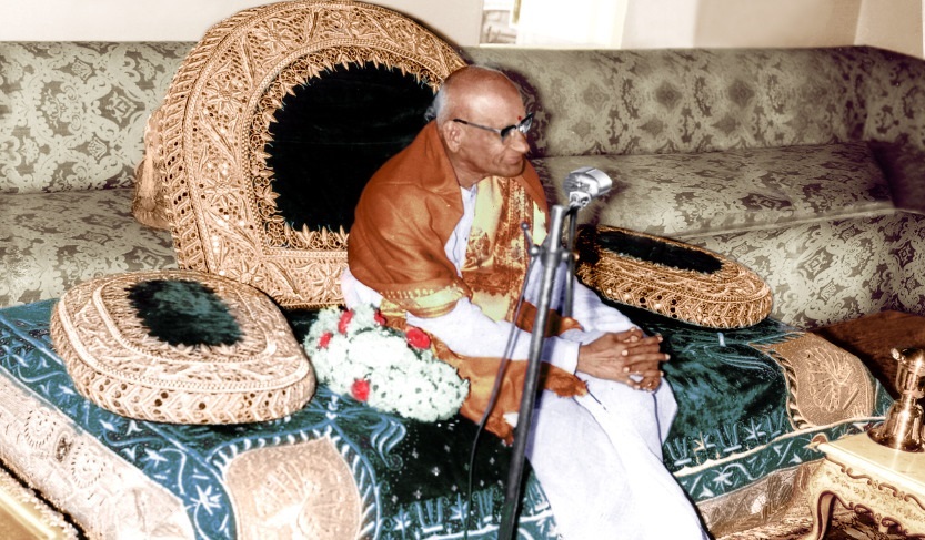Viswanatha Satyanarayana seated on a cushioned chair, speaking into a microphone