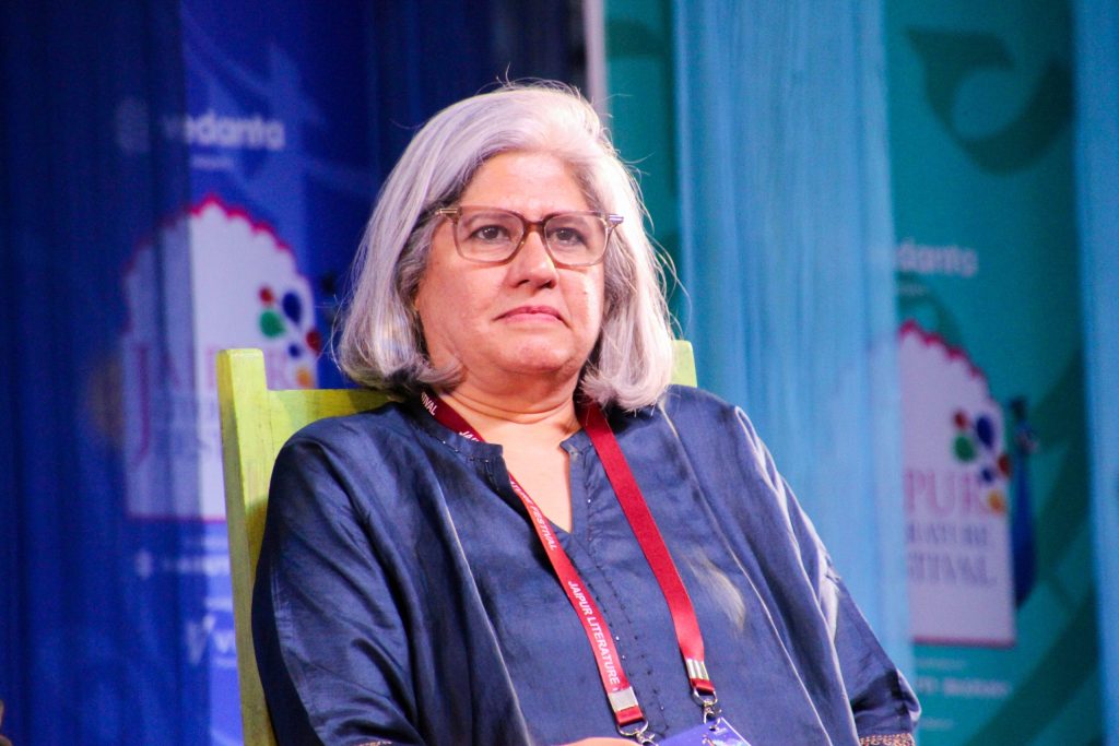 Vrinda Grover with grey hair and glasses, wearing a scarf, seated at a festival session