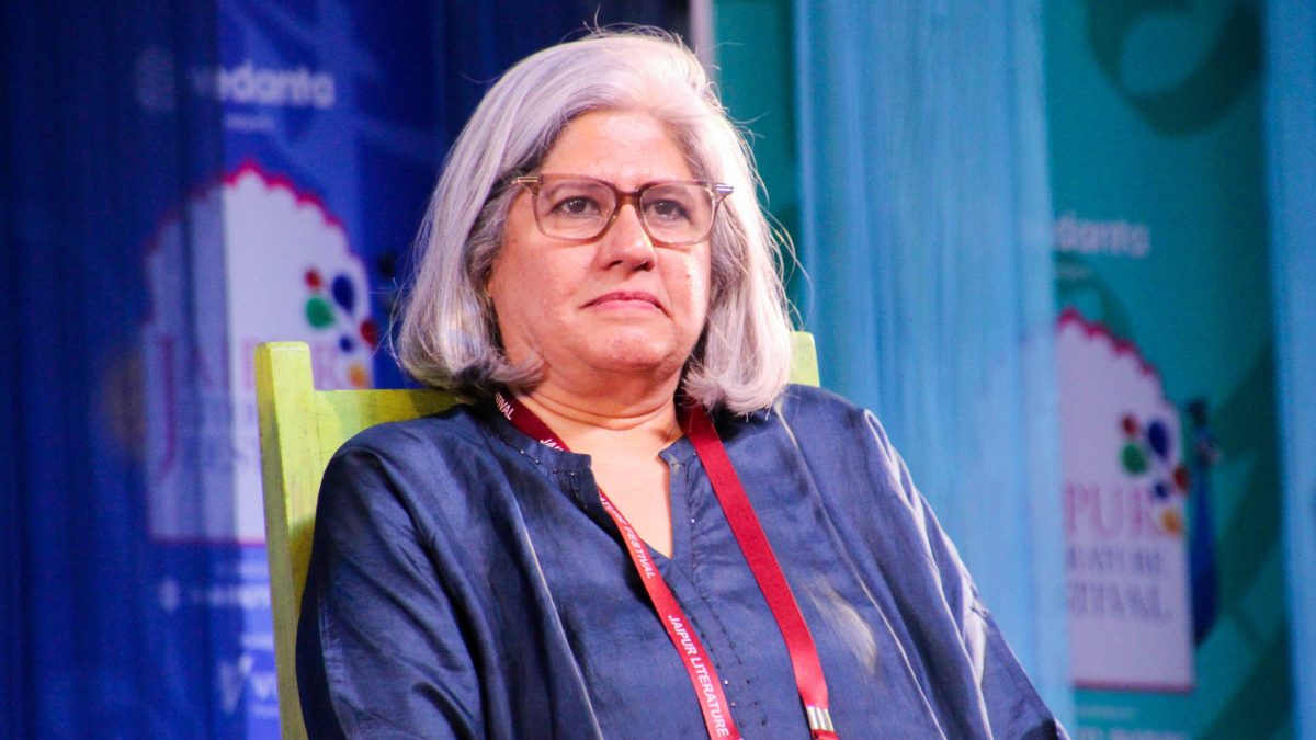 Vrinda Grover with grey hair and glasses, wearing a scarf, seated at a festival session