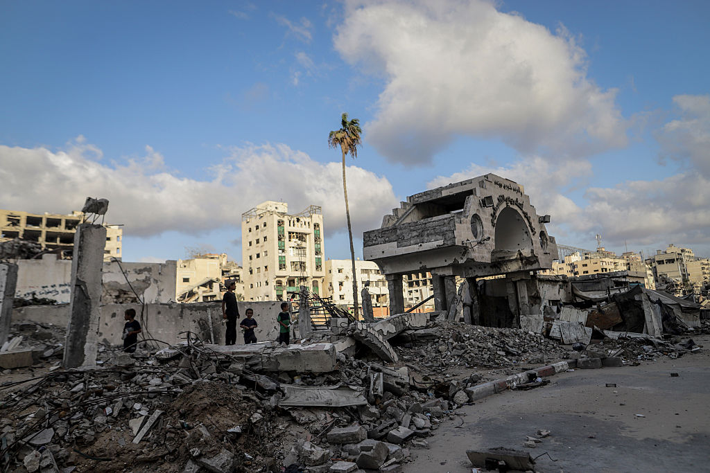 Children stand among rubble and destroyed buildings in a conflict zone in West Asia